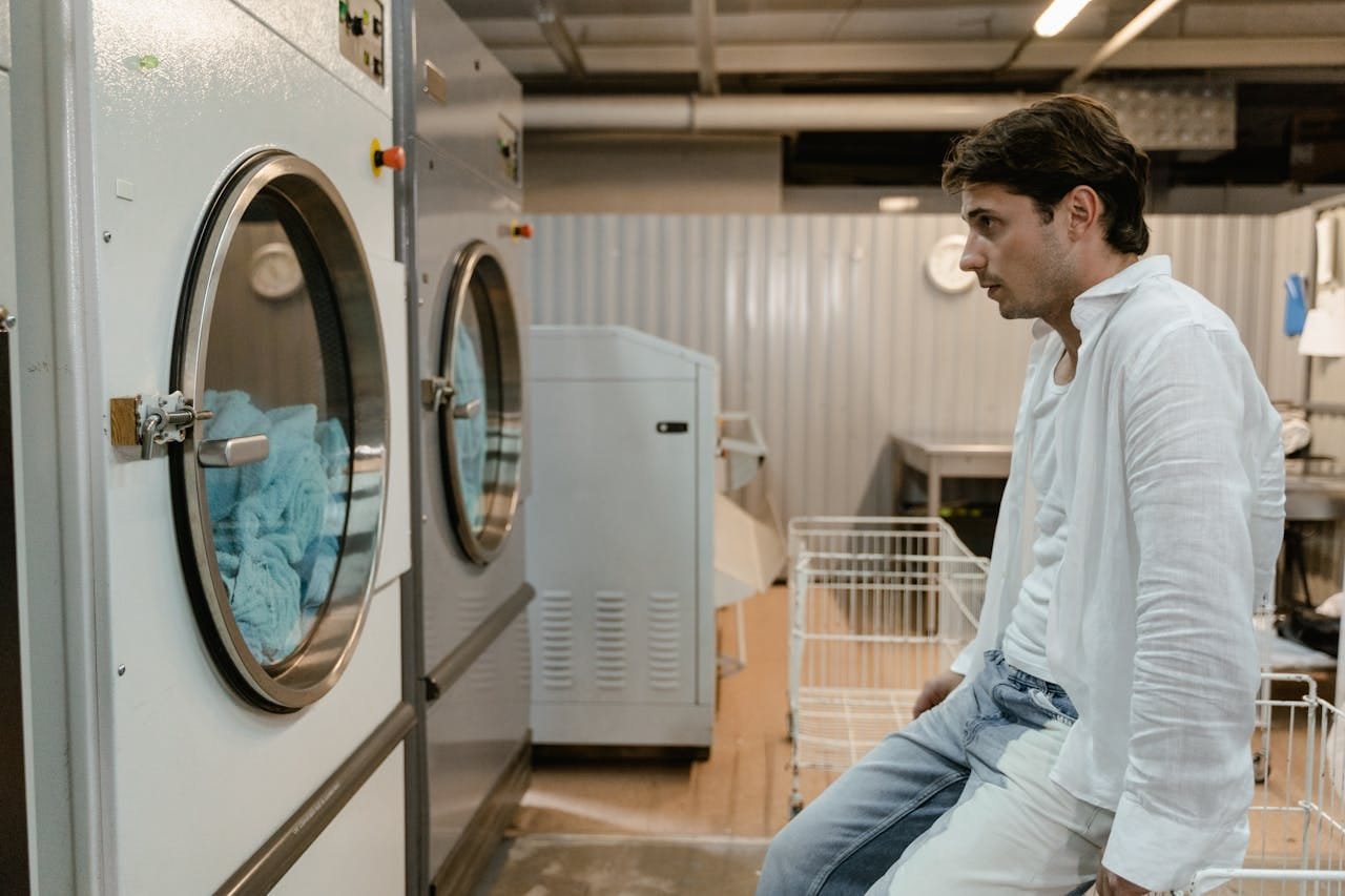 A man in a white shirt waits by machines in an industrial laundry facility.