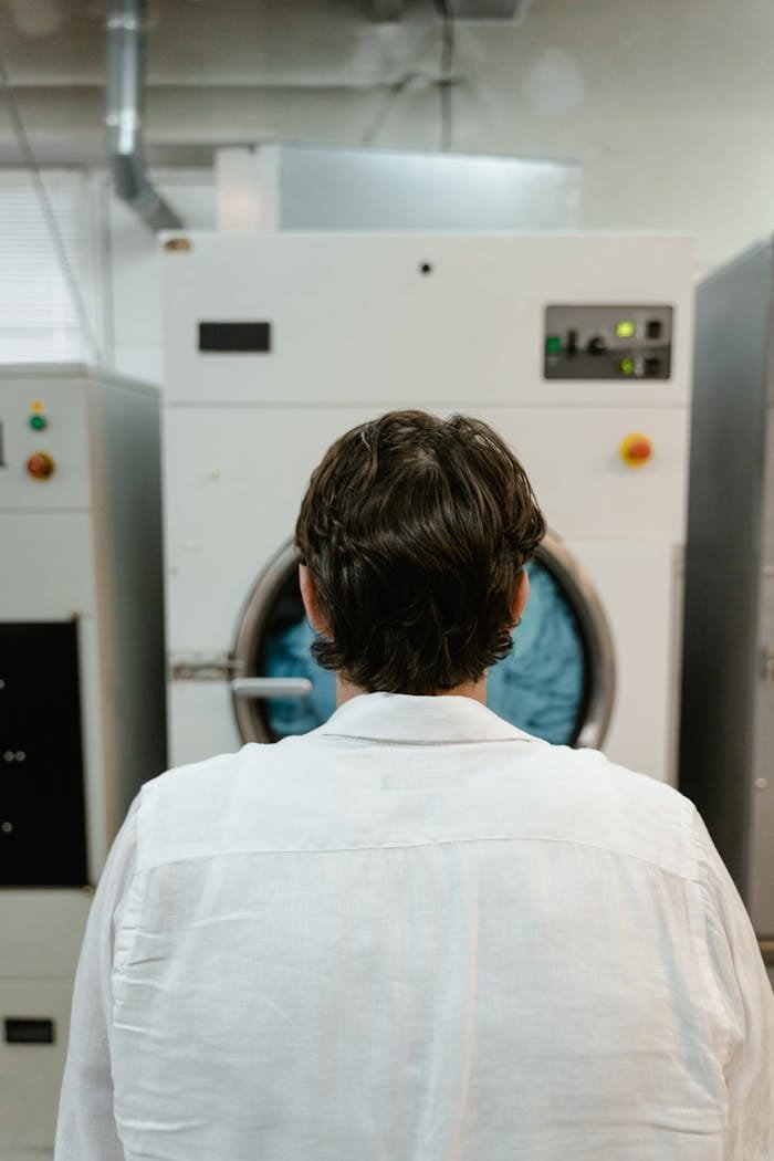 Back view of a man operating a large industrial washing machine in a laundry facility.